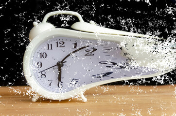 white alarm clock stands on a wooden table against a black wall, copy space. white alarm clock...