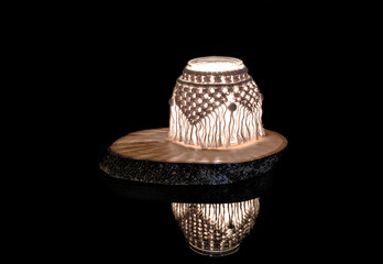 Hand made macrame candle holder on a wooden stand (rustic wood slice), with reflection, black background.