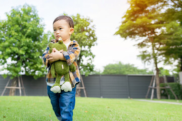 Cute little Asian boy is standing hugging his doll at the park,Happy and healthy childhood concept.