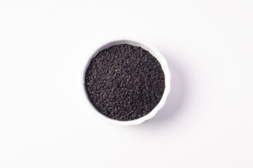 Black sesame seeds in a white ceramic cup on a white background