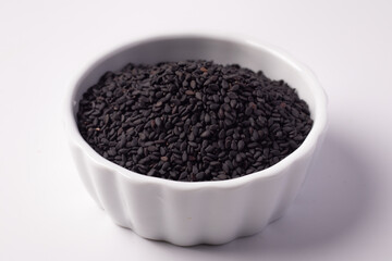 Black sesame seeds in a white ceramic cup on a white background
