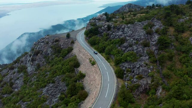 Aerial tilt revealing car driving on winding mountain road in Croatia