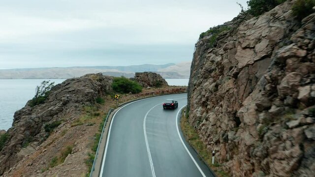 Black car drives around rocky mountain road in Karlobag, Croatia 