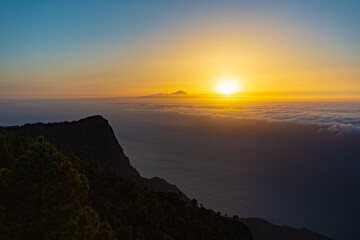 sunset from the canaries, the island of gran canaria with the roque faneque and the teide in the background bathed by a sea of clouds and the reflections and lux of the sun, in tamadaba natural park.