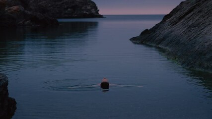 Cinematic and moody shot of young beautiful woman submerge into quiet water of secluded empty beach or cove. Mindfulness and tranquility concept, inner peace and self care at fancy spa on ocean