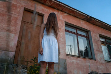 Fototapeta na wymiar girl in a white dress with long dark hair thrown over her face stands on the steps of an abandoned building. Concept of horror, mysticism