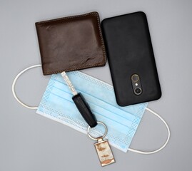 Car key, surgical mask, leather wallet and mobile phone on gray background.