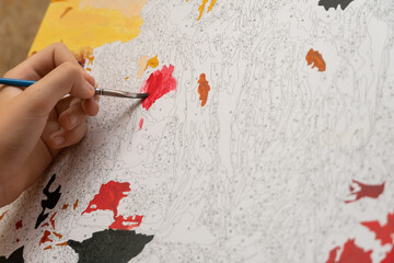 child's hand paints a picture by numbers close up with a red paint brush