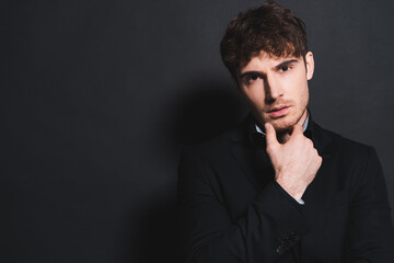 handsome man in formal wear looking at camera and touching face on black