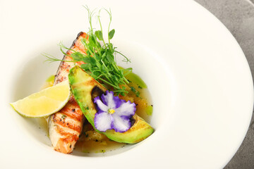 plate of grilled salmon steak with avocado and microgreen closeup