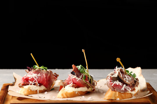set of traditional spanish tapas with beef on wooden deck and black background. topas or bruschetta with beef and microgreen