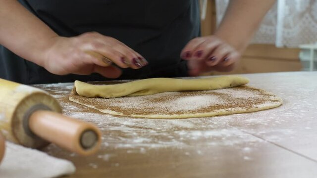 Close-up women's hands rolling up dough with cinnamon and sugar baking pastry at home, housewife cooking alone preparing pie cake or handmade danish cookies DIY bakery. rolling pin on table