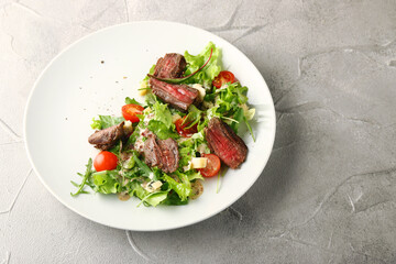 steak salad. Grilled Steak with Mixed Greed Salad cherry tomatoes and parmesan with fresh sauce in white plate on concrete background