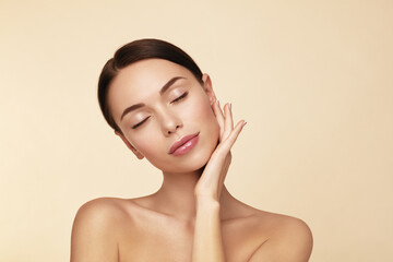 Softness. Beauty spa model closed eyes and touching her face against beige background.