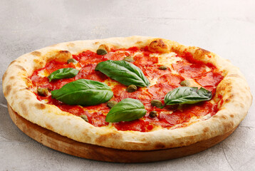 pepperoni pizza with capers and basil closeup on light concrete or stone table or background
