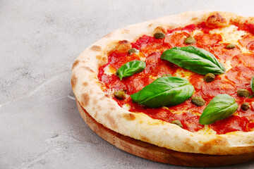 pepperoni pizza with capers and basil closeup on light concrete or stone table or background