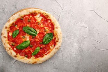 pepperoni pizza top view and basil closeup on light concrete or stone table or background. pizza with pepperoni, basil and capers