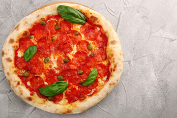 pepperoni pizza top view and basil closeup on light concrete or stone table or background. pizza with pepperoni, basil and capers