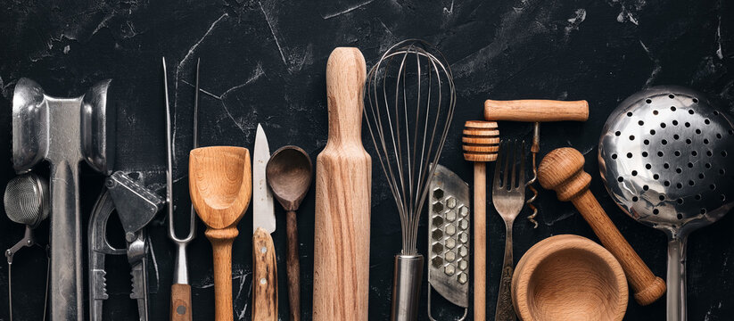 Various kitchen utensils and tools on a black stone background, banner. Top view, flat lay. Collection kitchenware.