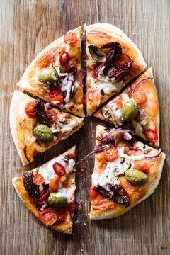 Vegan friendly homemade pizza topped with olives, plant based mozzarella and cherry tomatoes on a rustic oak chopping board