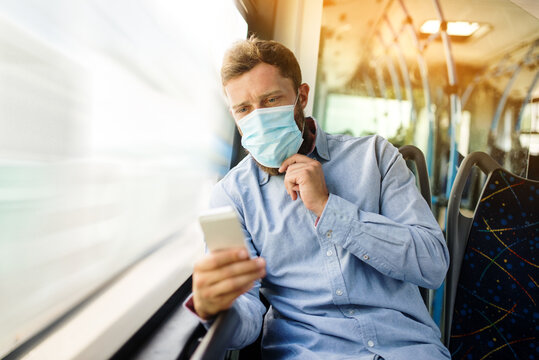 young man in a shirt with a mask on his face sits in a bus and uses a mobile phone