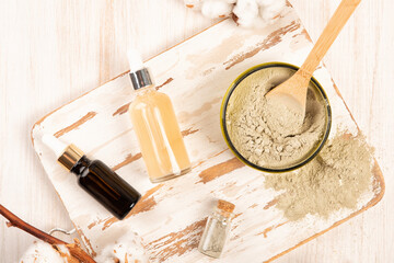 Dry facial clay powder mask in a jar and beauty essence bottles. Natural home cosmetic or spa treatment skincare on a wooden background