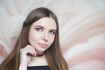 Young beautiful woman with brown makeup smoky eyes. Long straight hair, gathered hair-do. Professional make up, nude matte lips - waterproof lipstick. Dreamy blue eyes, touching her chin by fingers