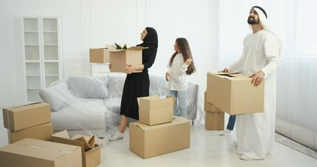 Arabian happy family with kids coming in new home and carrying carton boxes. Mother, father with kids entering house after repairment and looking around with smiles. Parents and children moving in.