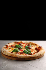 pizza with mushrooms, tomato and basil close up on light concrete or stone table and black background for copy space