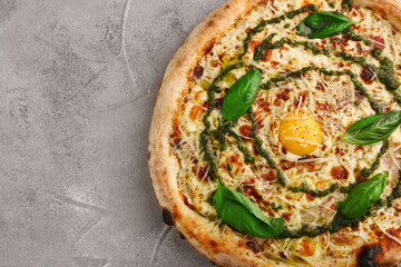 carbonara pizza with tomatoes, pesto, basil, mozzarella, parmesan and egg close up on gray concrete or stone background top view