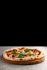 pizza with dried tomatoes, chicken, basil, tomatoes and mozzarella cheese close up on gray concrete or stone table and black background for copy space