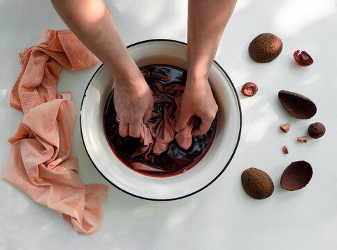 Woman's hand soaking fabric in pot with natural avocado dye, top view