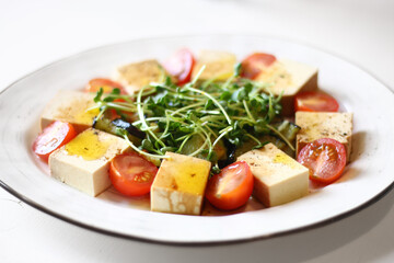 veggie salad with tofu, microgreen and cherry tomatoes close up on white table