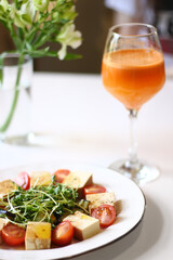 veggie salad with tofu, microgreen and cherry tomatoes and glass of carrot juice on white table