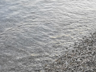 Pebble stones by the sea, diagonal water edge. Grey natural background with copy-space.