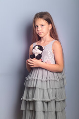 A beautiful long-haired girl with her favorite items in her hands on a light background in a gray dress with sequins. Foreground. Quarantine, games at home.