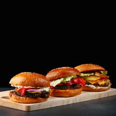 set of three burgers close up on wood and black isolated background for copy space. big tasty and juicy burgers concept