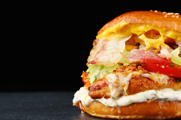 tasty burger with chicken and bacon on dark isolated background. Homemade hamburger or burger with fresh vegetables and cheese