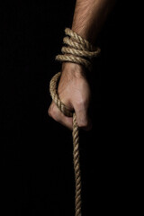 Male hand holds a rope on a black background. Jute rope wraps around the arm.
