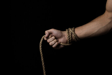 Male hand holds a rope on a black background. Jute rope wraps around the arm.