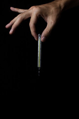 A man's hand holds a thermometer on a black background. Thermometer for measuring human temperature