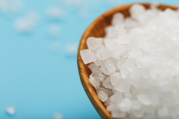 In a wooden spoon, sea salt crystals on a blue background, macro.