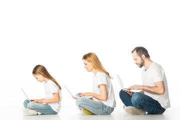 side view of family sitting on floor with laptops on crossed legs isolated on white
