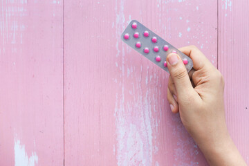 Top view of women hand holding blister pack on pink background 