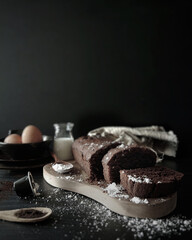 Chocolate Pound Cake with Ingredients, shot against Black background. Dark food photography for chocolate cake on a wooden chopping board.