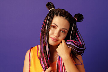 Naklejka na ściany i meble Smiling positive young woman with colorful african braids on purple background