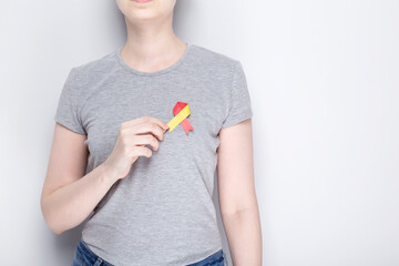 World Hepatitis Day concept. Girl in gray T-shirt holds in her hand awareness symbol red-yellow ribbon. Gray background. Copy space