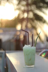 Chendol Cocktail. Singapore cocktail on a bar top taken against the sunset abd trees with natural lens flare. Asian inspired cocktail.