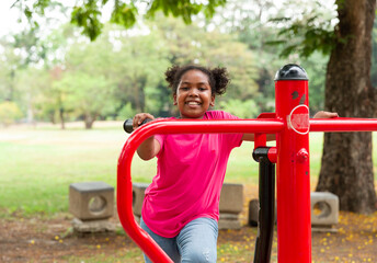 Fototapeta premium Cute Afro little girl with curly hair playing at the playground in the garden