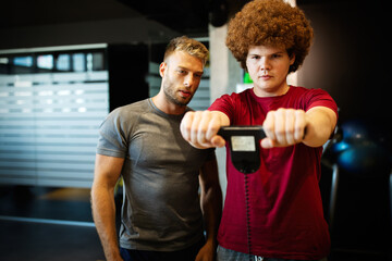 Fat young men with trainer exercising at fitness gym.